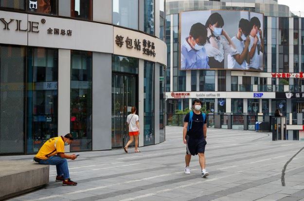 رجل يضع كمامة يسير بالقرب من شاشة تعرض تذكيرا للناس بضرورة وضع الكمامات في بكين. تصوير: توماس بيتر - رويترز